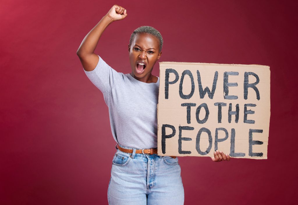 Femme levant le poing et tenant une pancarte "Power to the People" devant un fond rouge