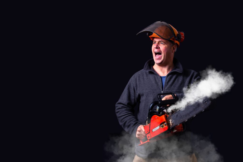 Homme portant un casque de sécurité utilisant une tronçonneuse avec de la fumée.